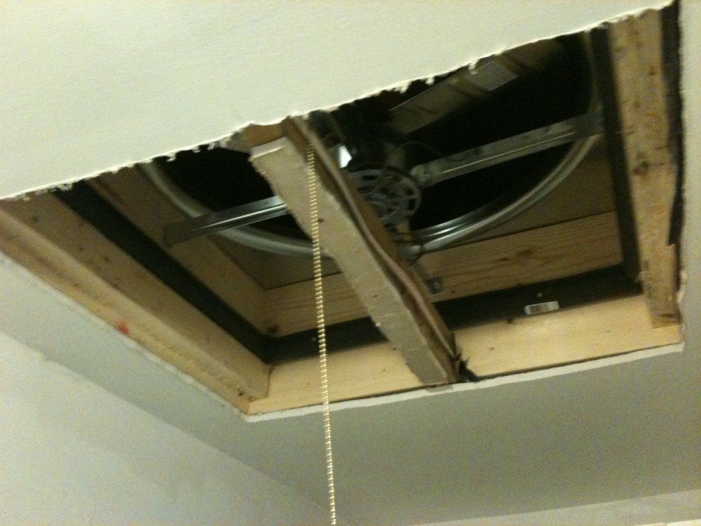 Picture of the ceiling with a hole in it for a whole house fan.  The fan is installed without shutters so you can see the foam pipe insulation between the fan and the supporting boards.